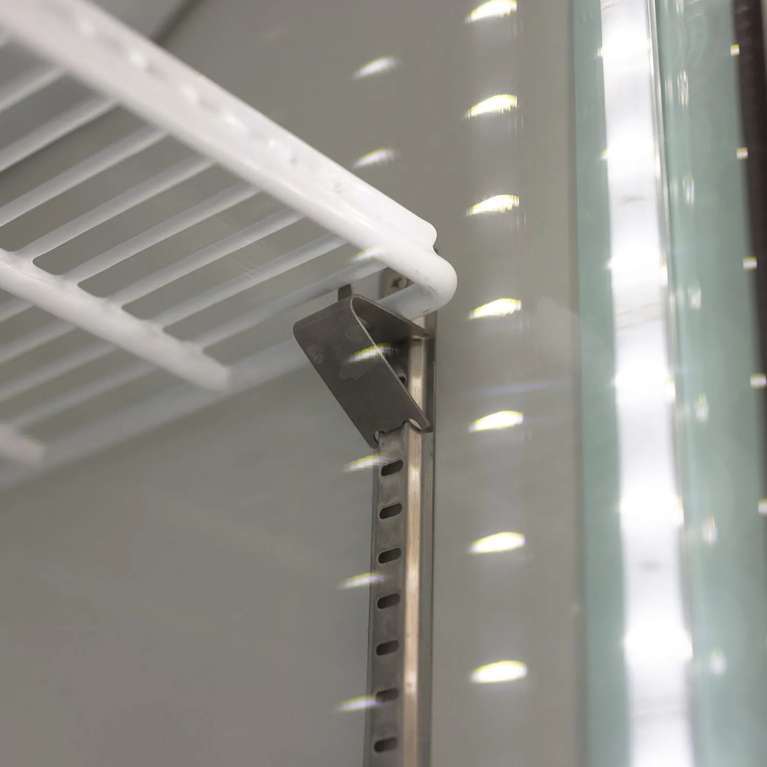 Close-up of a white shelf inside a refrigerator with a metal bracket.