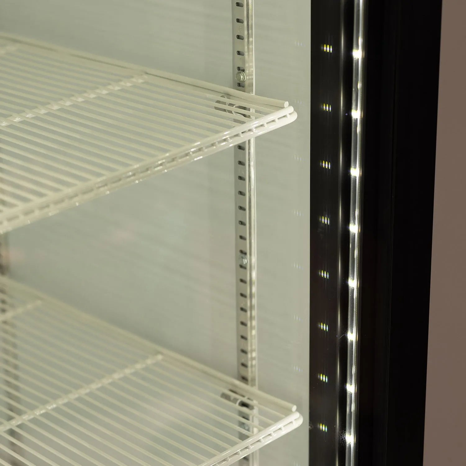 Metal shelving unit next to a refrigerator with illuminated interior.